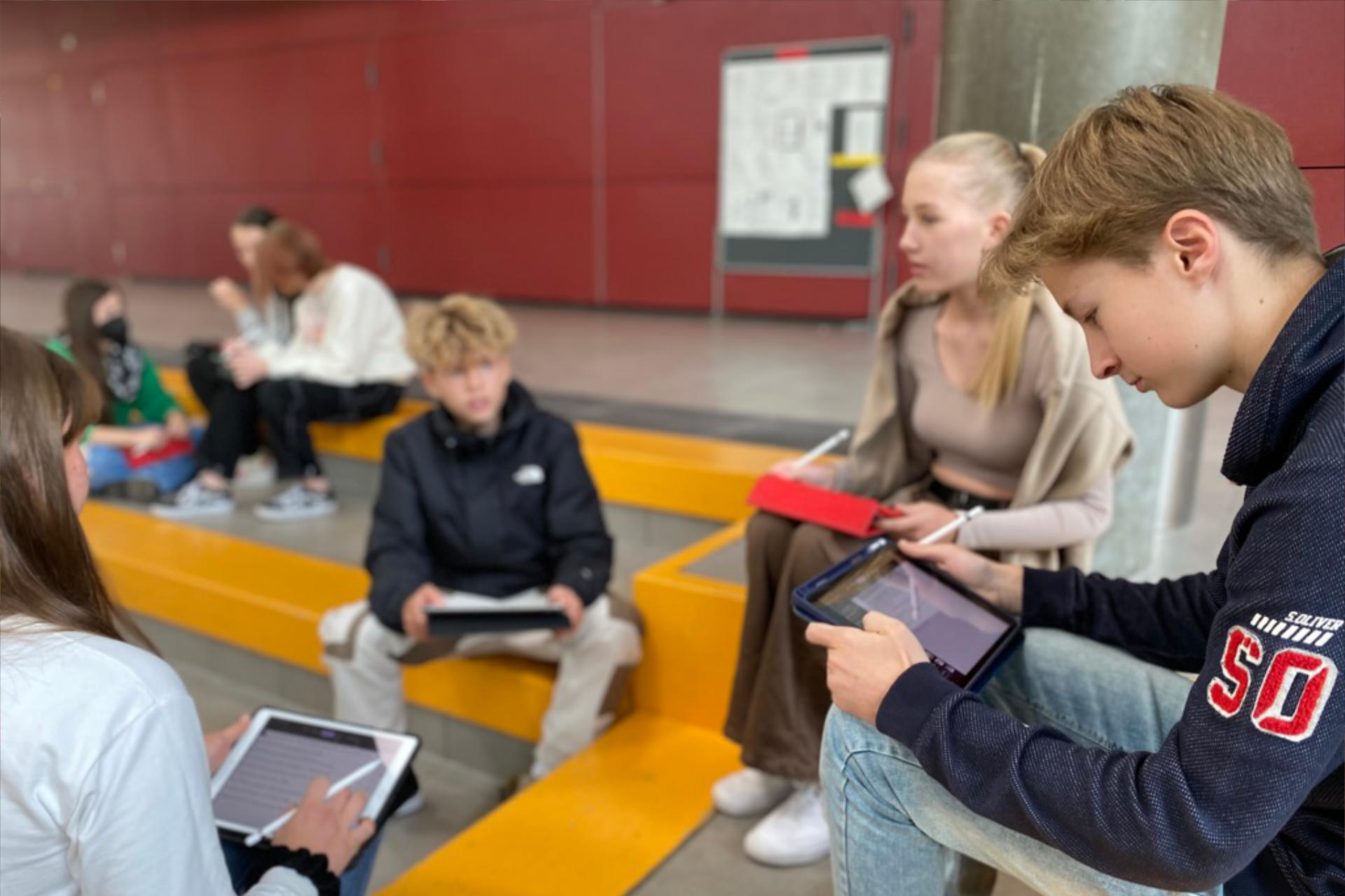 Schülerinnen und Schüler lernen mit iPads in der Aula der Adolf-Reichwein-Schule.