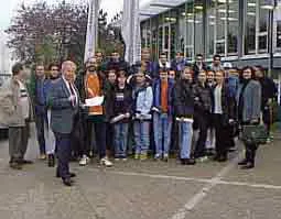 Eine Gruppe Jugendlicher steht mit einem Mann im Anzug vor der Glasfassade eines Gebäudes.