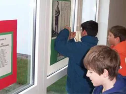Kinder stehen an einer Glaswand und heften Zettel an eine Stellwand.