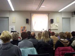 Zuhörer sitzen dicht gedrängt in einem Raum vor einer Leinwand.