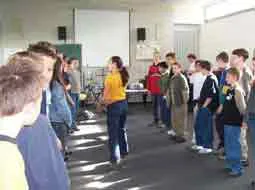 Kinder stehen in einer langen Reihe an aneinandergestellten Tischen im Klassenraum.