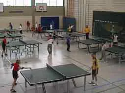 In der Sporthalle stehen mehrere Tischtennisplatten, an denen Kinder spielen.