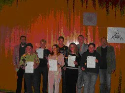 Die Preisträger halten ihre Urkunden vor einem großflächigen roten Wandbild.
