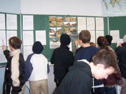 Kinder stehen an einer Pinnwand im Klassenraum und tragen Ergebnisse ein.