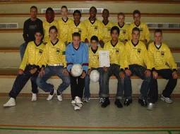 Die Fußballmannschaft in gelben Trikots sitzt mit Urkunde und Bällen in der Halle.