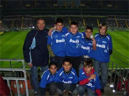 Jungen in blauen Trikots stehen auf der Tribüne eines Fußballstadions.