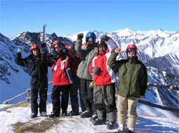 Jugendliche mit Skihelmen jubeln vor einer verschneiten Bergkulisse.