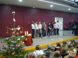 Bei der Adventsandacht stehen Kinder vor dem geschmückten Weihnachtsbaum in der Aula.