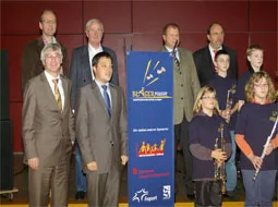 Sponsoren und Schulvertreter stehen mit Kindern und ihren Blasinstrumenten vor einem Banner.