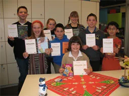 Kinder halten ihre Urkunden und Buchpreise über einen weihnachtlich gedeckten Tisch.