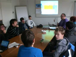 Jugendliche sitzen um einen Tisch mit Beamer und folgen der Präsentation.