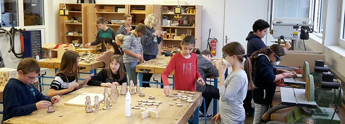 Kinder arbeiten in der Holzwerkstatt der Schule an Werkbänken und gestalten kleine Holzfiguren.