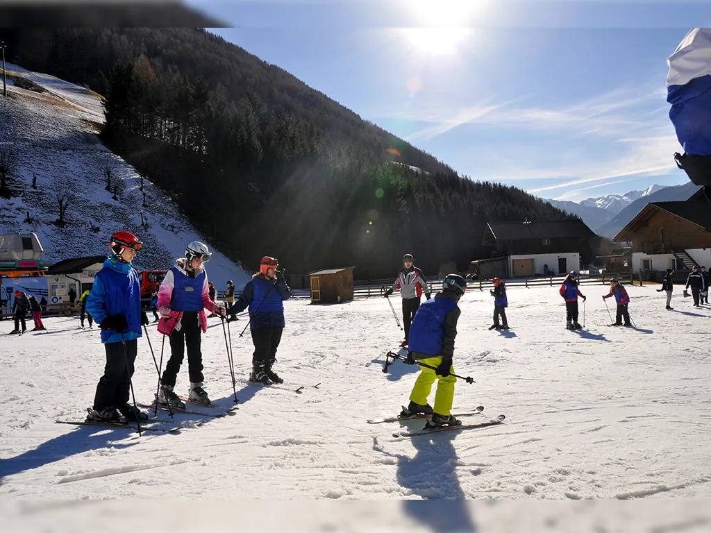 Jugendliche in Skikleidung stehen bei Sonnenschein mit Skiern und Stöcken auf einer flachen Piste im Ahrntal.
