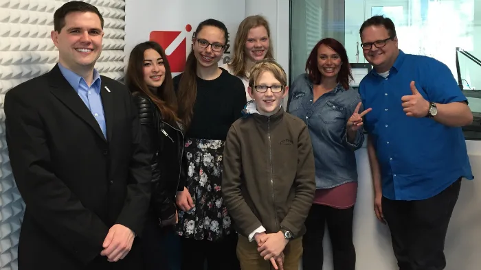 Schülerinnen und Schüler des Schulradios stehen mit zwei Erwachsenen im Funkhaus von Antenne Mainz, einer der beiden zeigt den Daumen nach oben.