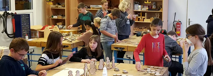 Kinder arbeiten in der Holzwerkstatt der Schule an Werkbänken und gestalten kleine Holzfiguren.