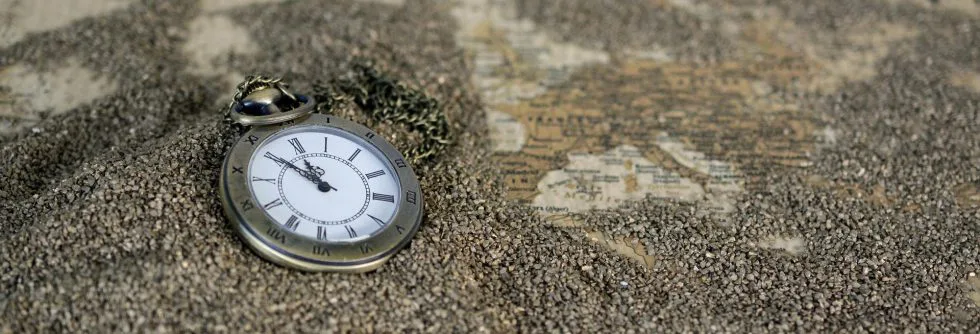 Eine alte Taschenuhr liegt halb im Sand vergraben – das Motiv des Theaterabends zum Thema Zeit.