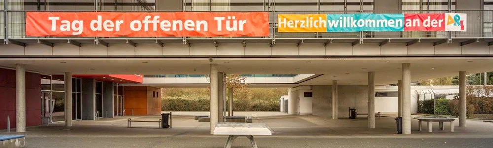 Über dem Eingang der Schule hängt ein orangefarbenes Banner mit der Aufschrift „Tag der offenen Tür“ und „Herzlich willkommen an der ARS“.