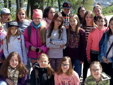 Eine Gruppe Kinder posiert bei einem Ausflug im Freien; im Hintergrund ein bewaldeter Hang und ein Flusstal.
