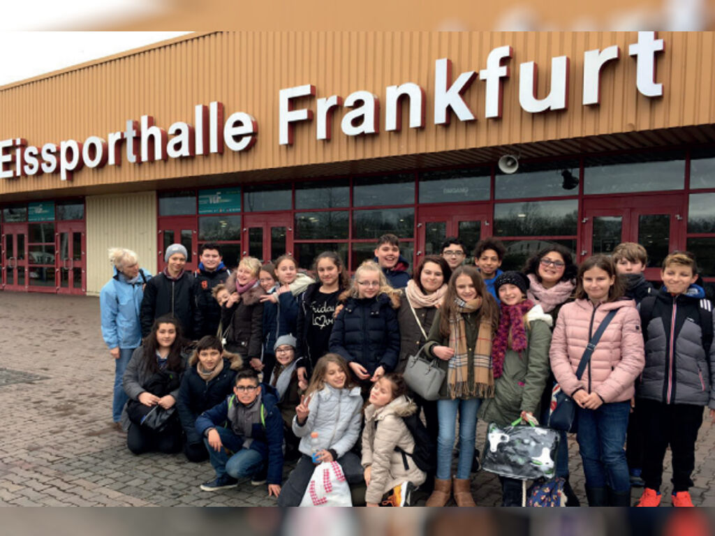 Eine große Gruppe Kinder posiert vor dem Gebäude der Eissporthalle Frankfurt mit dem großen Schriftzug „Eissporthalle Frankfurt“ an der Fassade.