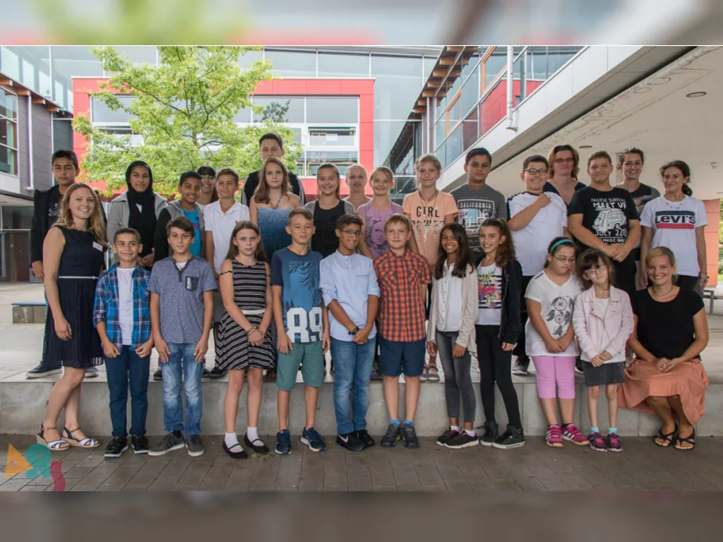 Eine neue fünfte Klasse steht mit ihren Lehrkräften für das Klassenfoto im Schulhof.