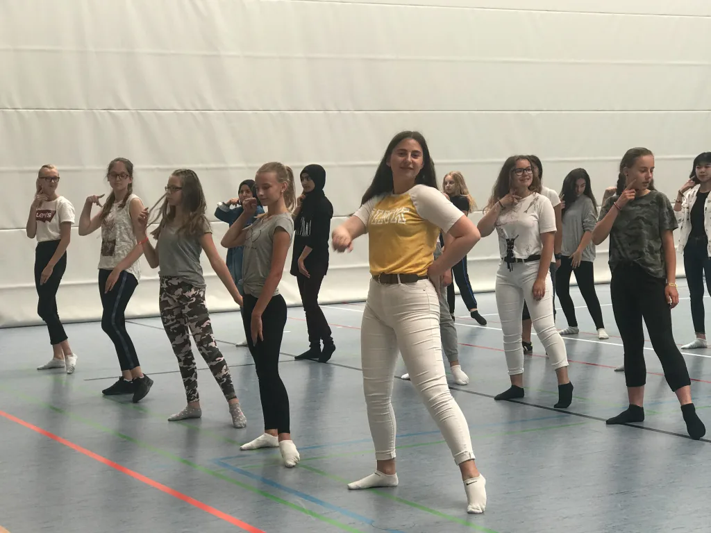 Tanzgruppe probt in Reihen in der Sporthalle.