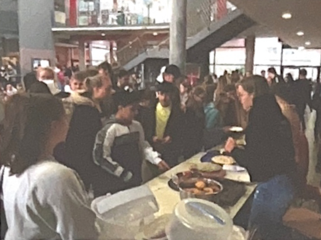 Reges Treiben an einem Verkaufstisch im Schulforum: Jugendliche drängen sich um einen Tisch mit Kuchen und Tellern.
