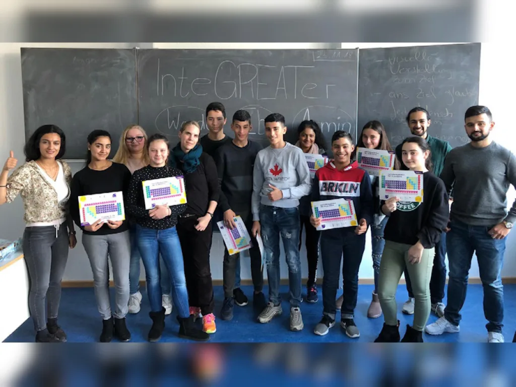 Die Gruppe steht mit Urkunden vor der Tafel mit dem Schriftzug „InteGREATer“.
