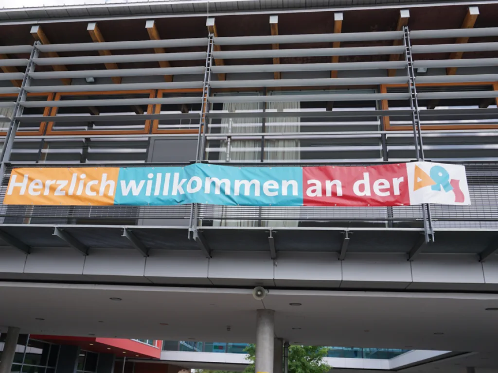 Banner mit der Aufschrift „Herzlich willkommen an der“ am Schulgebäude.