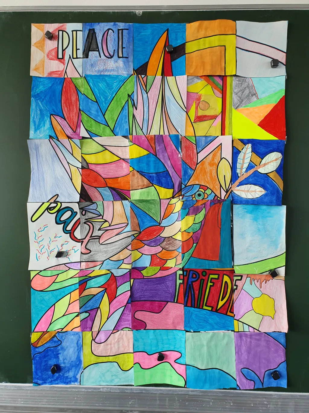 Ein großflächiges Gemeinschaftsbild aus vielen bunt bemalten Einzelblättern an der Wand, darauf die Wörter „Peace“, „Paix“ und „Frieden“.