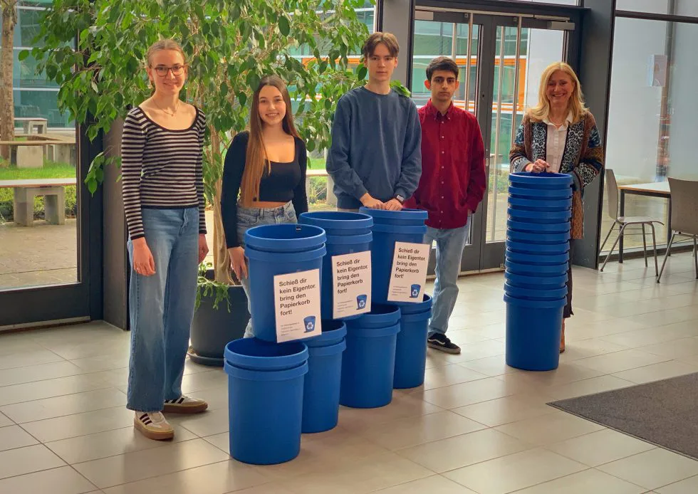 Fünf Jugendliche der Schülervertretung stehen im Foyer neben neuen blauen Sammelbehältern für die Mülltrennung.