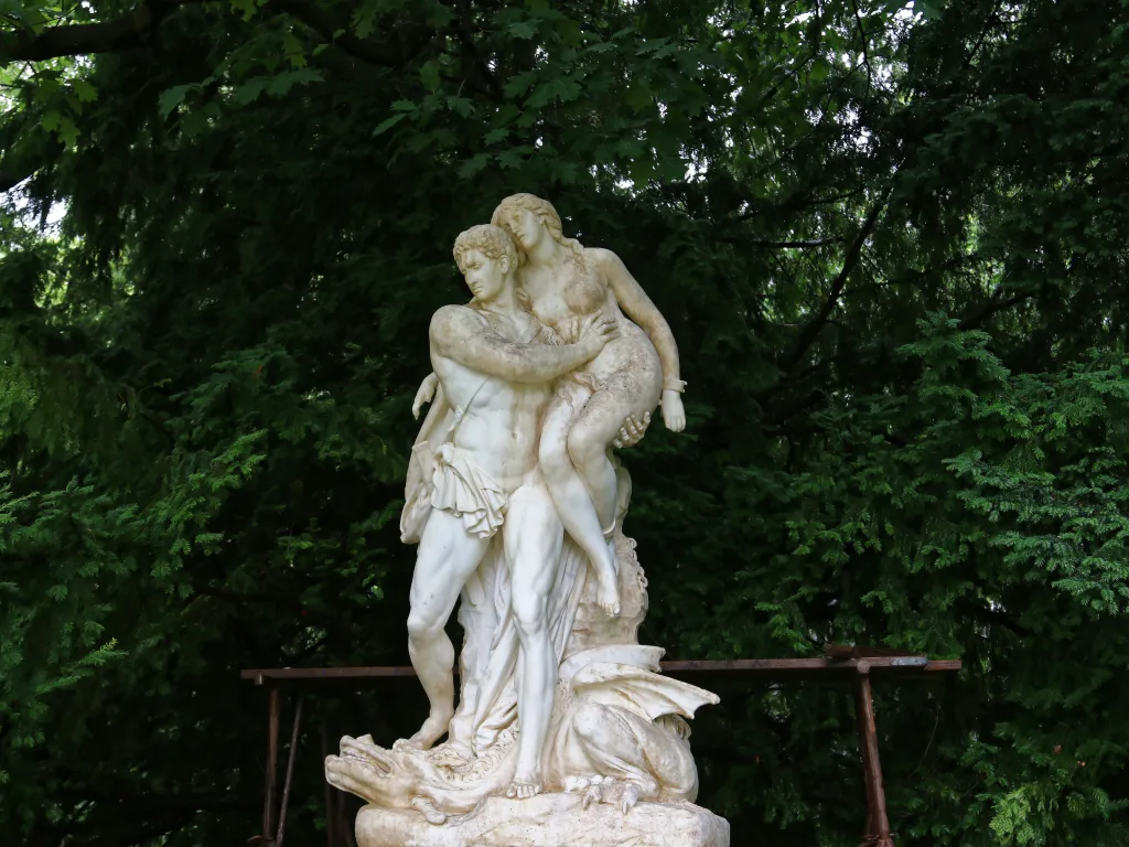 Steinerne Figurengruppe im Park vor dunklen Bäumen.