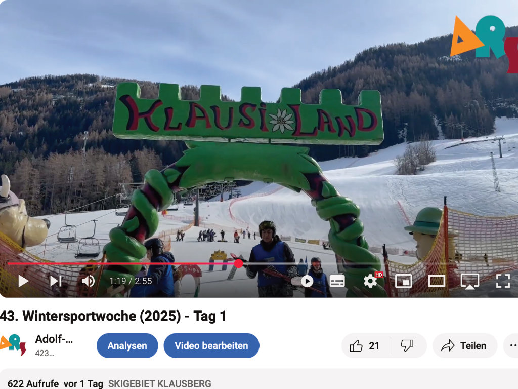 Standbild eines YouTube-Videos „43. Wintersportwoche (2025) – Tag 1“: ein grüner „Klausiland“-Torbogen am Eingang eines Skigebiets mit Sessellift und verschneiter Piste.