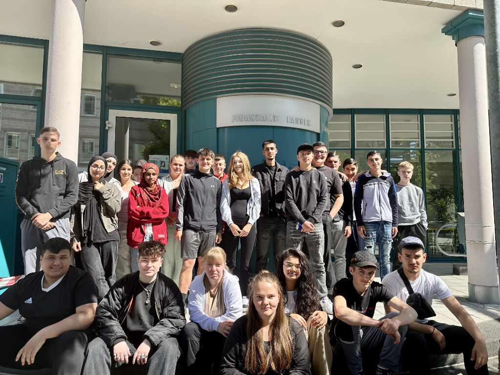 Eine große Schülergruppe posiert vor dem Eingang des Finanzamts Langen mit dem Schriftzug „Finanzamt Langen“ an der Fassade.
