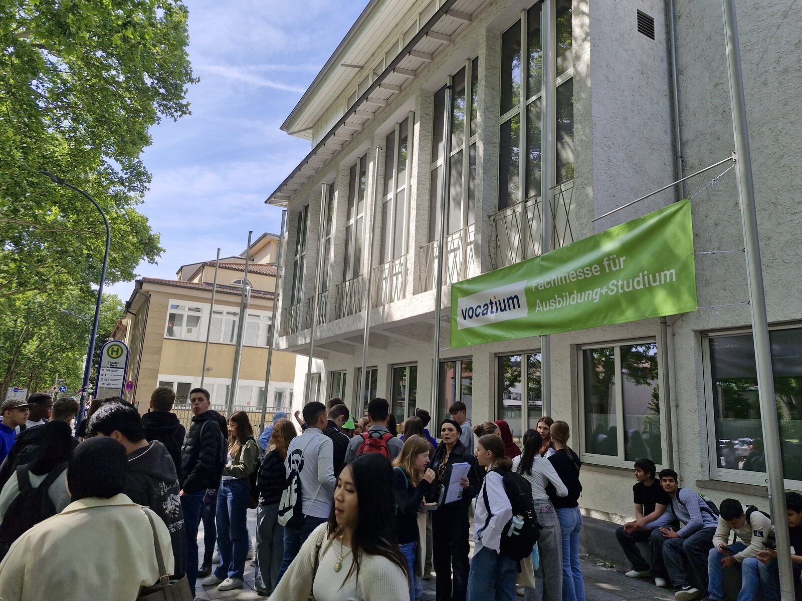 Das Bild zeigt einen Computerbildschirm mit einem Artikel über eine Berufsmesse. In der Mitte ist ein Foto von vielen Jugendlichen, die draußen vor einem Gebäude stehen und sich informieren. Man sieht Logos und Banner der Messe „vocatium“. Darunter steht ein Text darüber, dass die Jugendlichen die Messe besucht haben, um sich über Berufe und Studienmöglichkeiten zu informieren. Rechts ist ein kleines Porträt einer Ansprechperson.