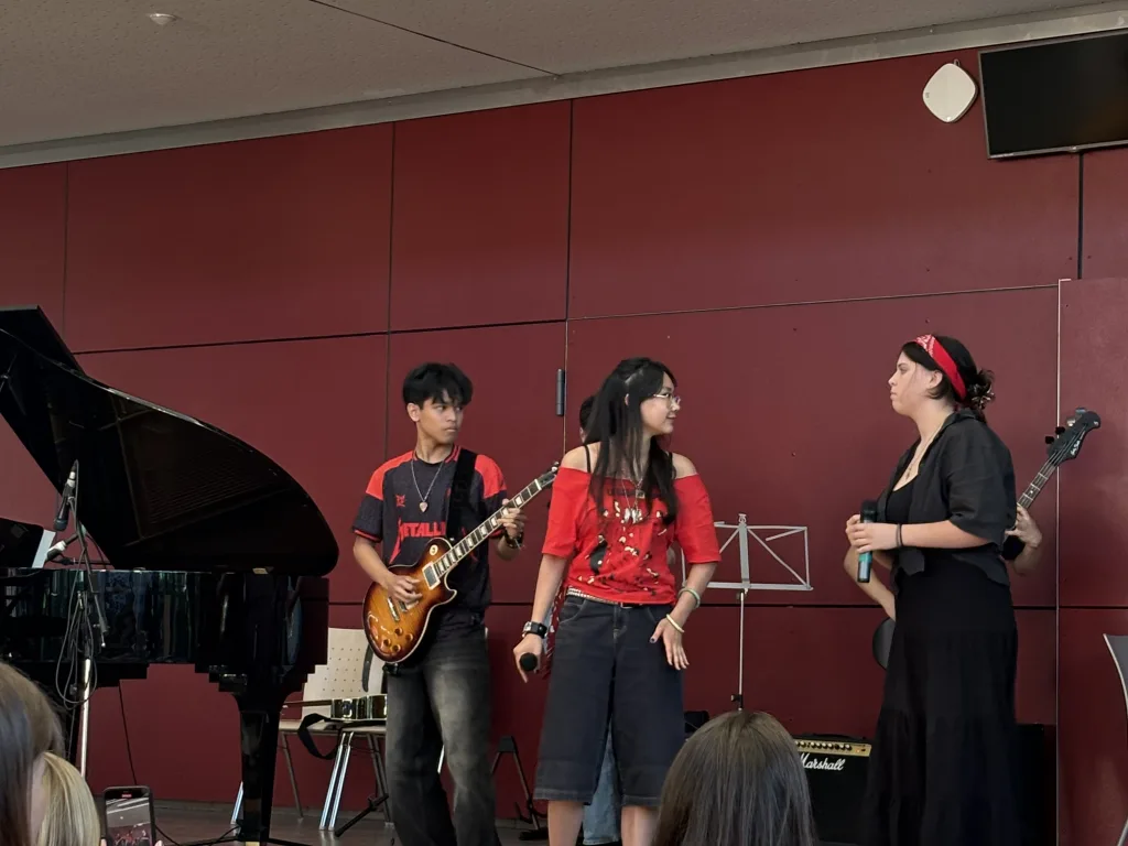 Die Schulband in roten Trikots spielt Gitarre und singt.
