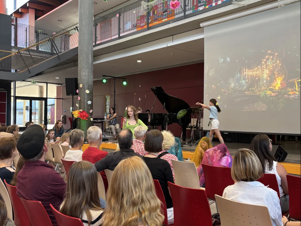 Blick über das Publikum zur Bühne mit Leinwand.