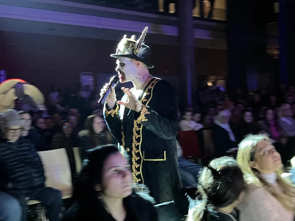 Ein Sänger in Kostüm und Krone singt ins Mikrofon, davor das Publikum.