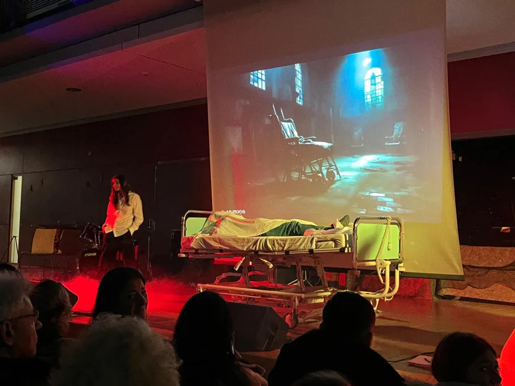 Eine Bühnenszene mit Liege und Projektion in rotem Licht.