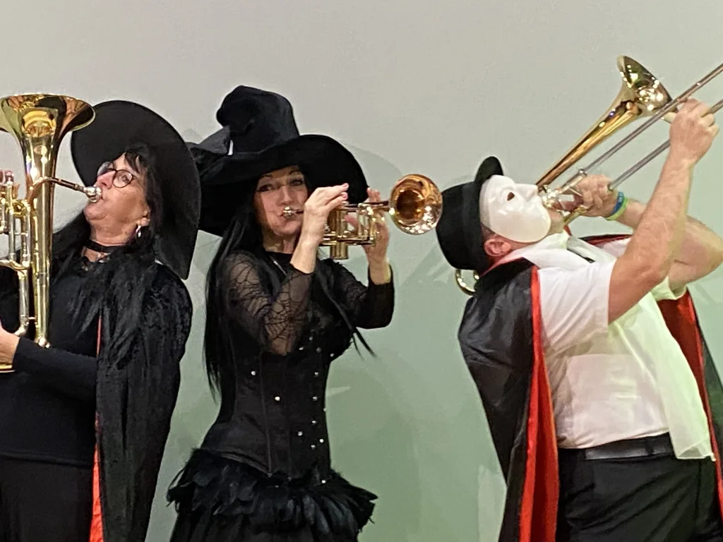 Drei Blechbläser in Halloween-Kostümen spielen Trompete und Posaune.
