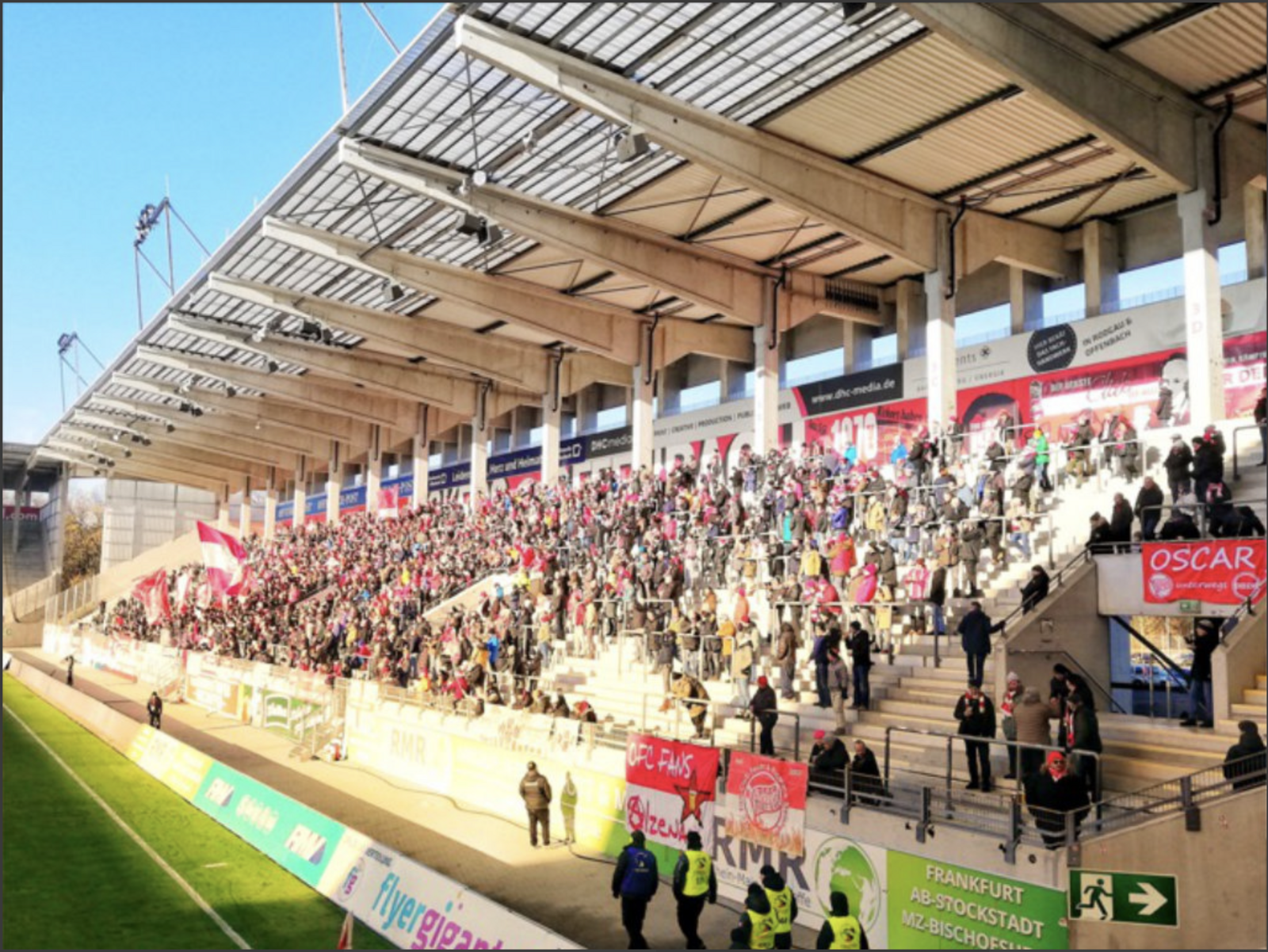 Die gut gefüllte Tribüne des Stadions am Bieberer Berg mit zahlreichen Fans, roten Fahnen und Bannern.