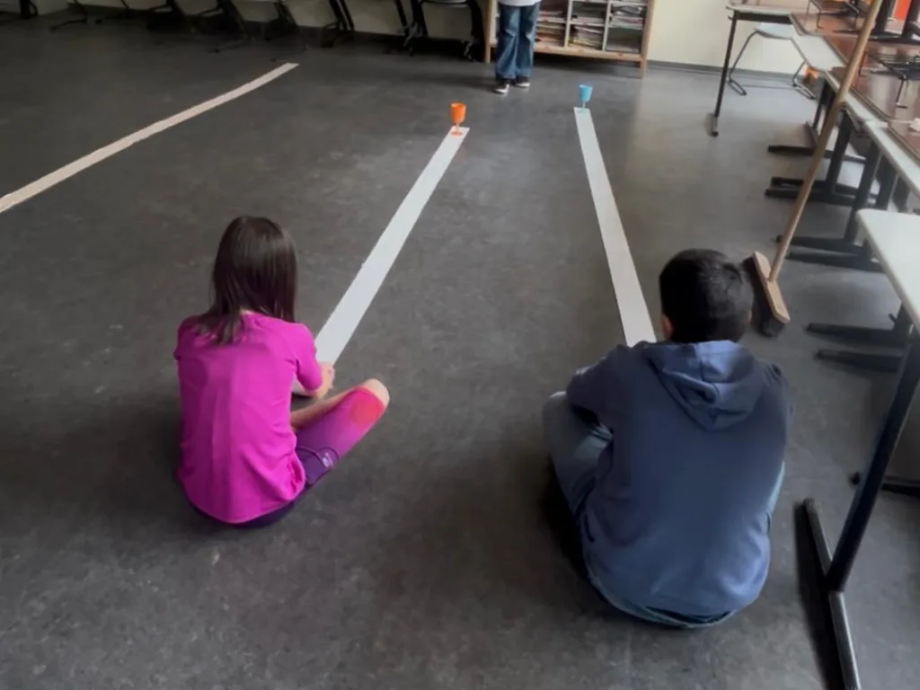 Zwei Kinder sitzen sich an einer Bahn aus Klebeband gegenüber und spielen.