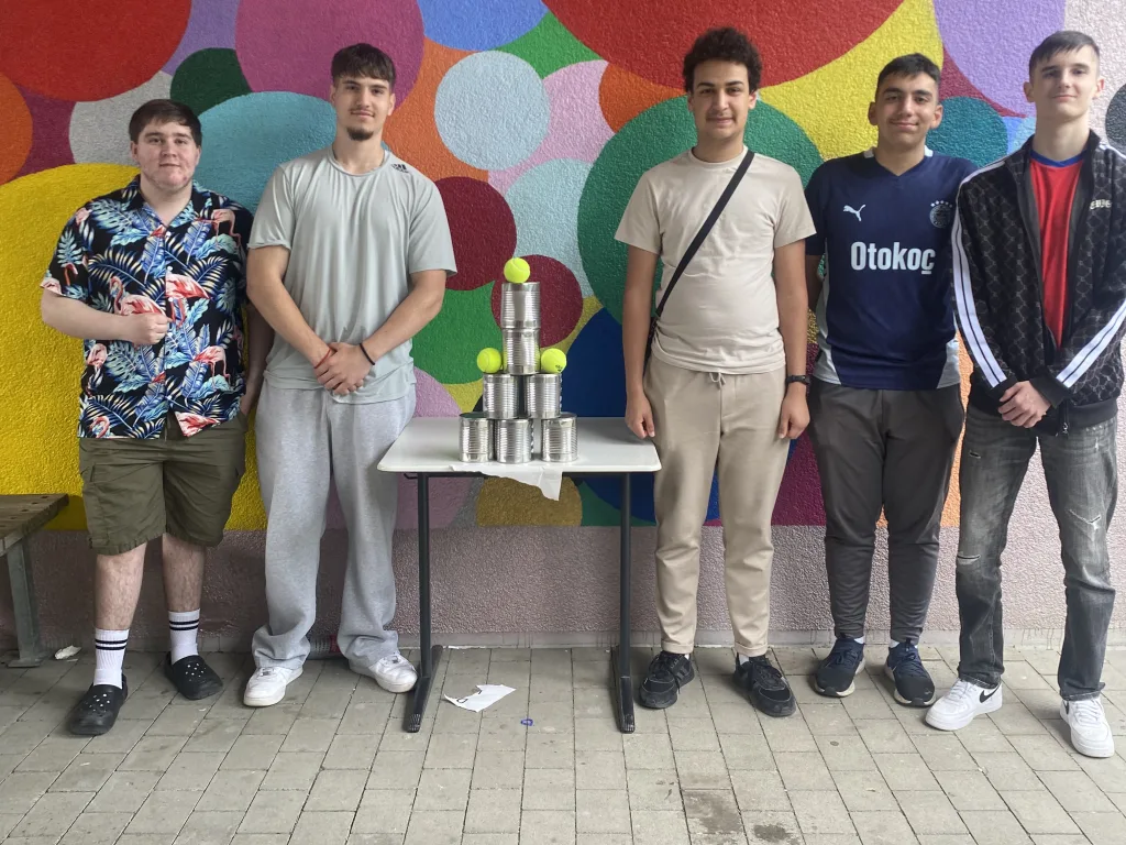 Fünf Jugendliche stehen vor einer bunt bemalten Wand an einem Spieltisch.