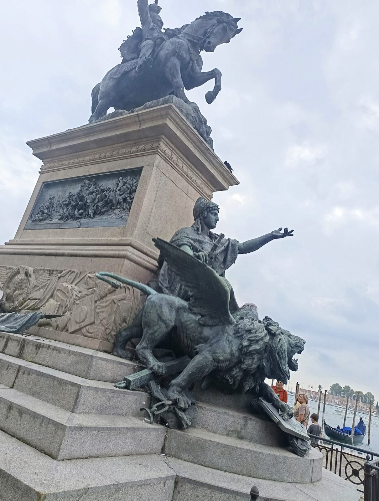 Das bronzene Reiterdenkmal für Viktor Emanuel II. in Venedig mit einem geflügelten Löwen am Sockel; im Hintergrund die Lagune mit Gondeln.