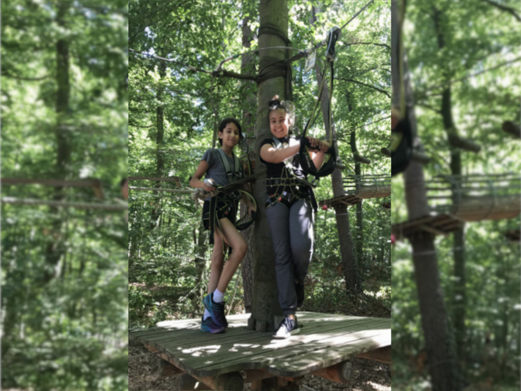 Schülerinnen und Schüler stehen auf einer Holzplattform im Kletterwald und blicken mit ihrer Kletterausrüstung in die Kamera.