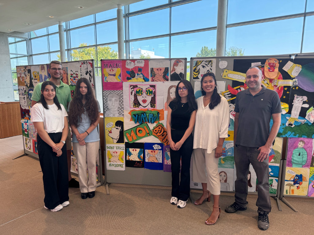 Drei Schülerinnen stehen mit den verantwortlichen Lehrkräften, Frau Nguyen und Herrn Matsche-Marian, und Herrn Becker vor den Kunstwerken.
